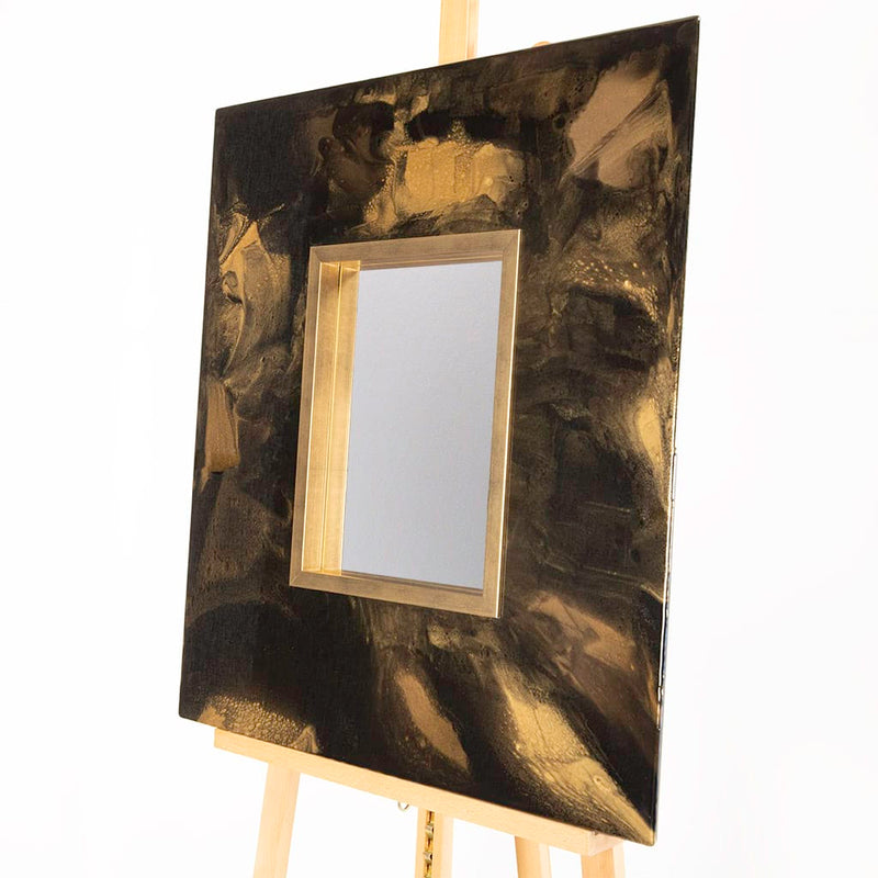 Angled view of a handmade abstract resin wall mirror featuring black and gold metallic textures, a brushed gold frame and contemporary luxury design for modern interiors.